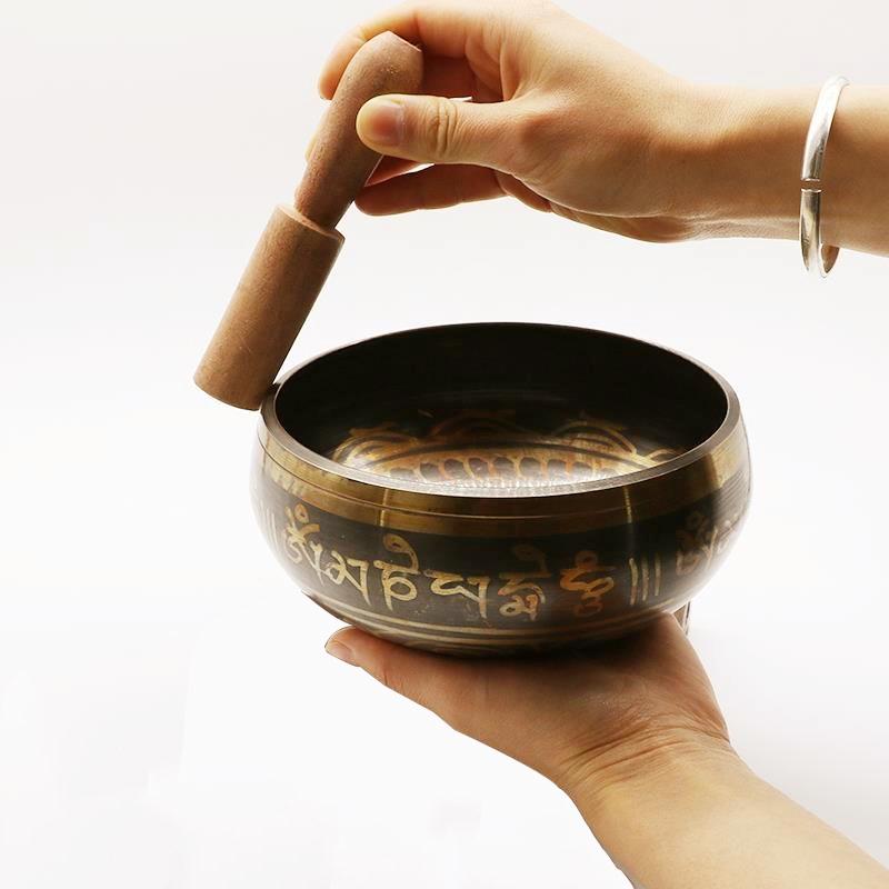 A woman holds a singing bowl in one hand, and with the other runs the striker around the edge