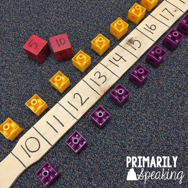 Wooden paint stirrer stick divided into squares labeled with numbers from 10 to 20, with colored cubes next to each square and a pair of dice