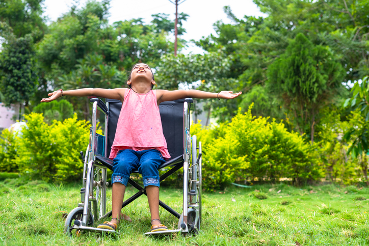 A girl in a wheelchair stretches her arms wide and tilts her head to the sky