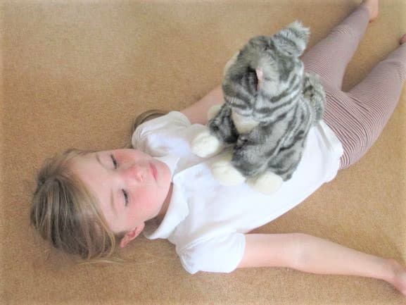 A young student lies on the floor with a stuffed animal on her chest